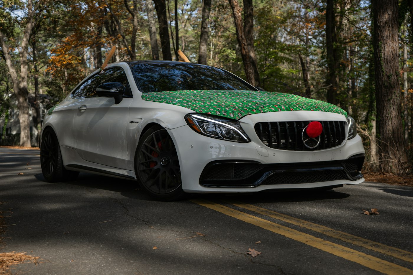 A white car driving down a street next to a forest